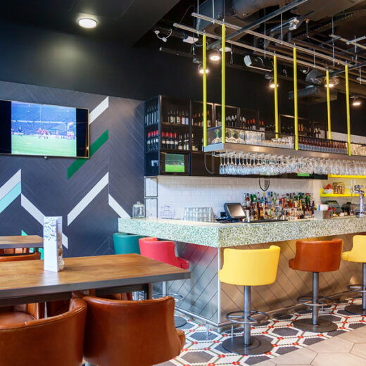 Modern restaurant bar with mounted TV, clean AV display, pendant lighting, and tabletop and bar seating.