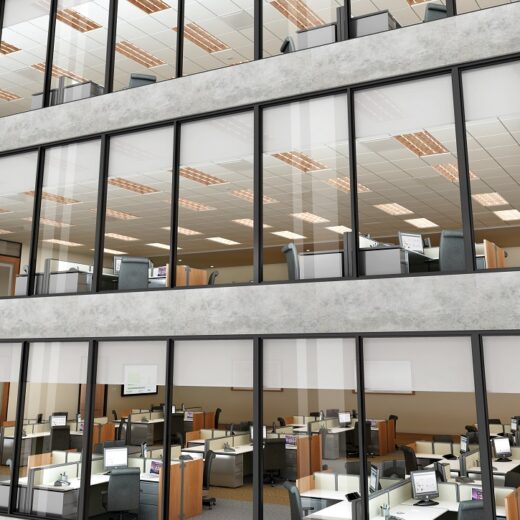 Exterior shot of a commercial building featuring three distinct floors of cubicles with shades closed a fourth of the way down on all the windows.