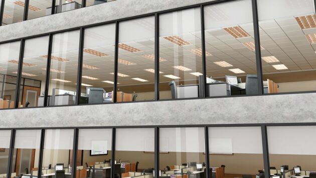 Exterior shot of a commercial building featuring three distinct floors of cubicles with shades closed a fourth of the way down on all the windows.