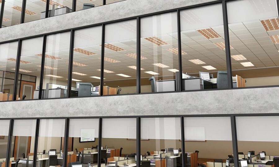 Exterior shot of a commercial building featuring three distinct floors of cubicles with shades closed a fourth of the way down on all the windows.