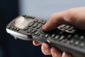 A hand operating a universal-style AV remote control.