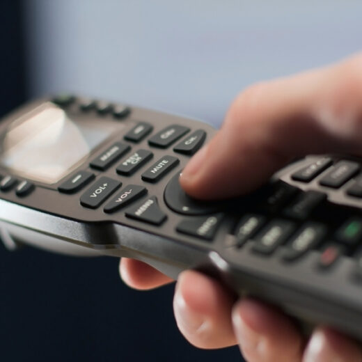A hand operating a universal-style AV remote control.
