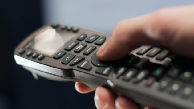 A hand operating a universal-style AV remote control.
