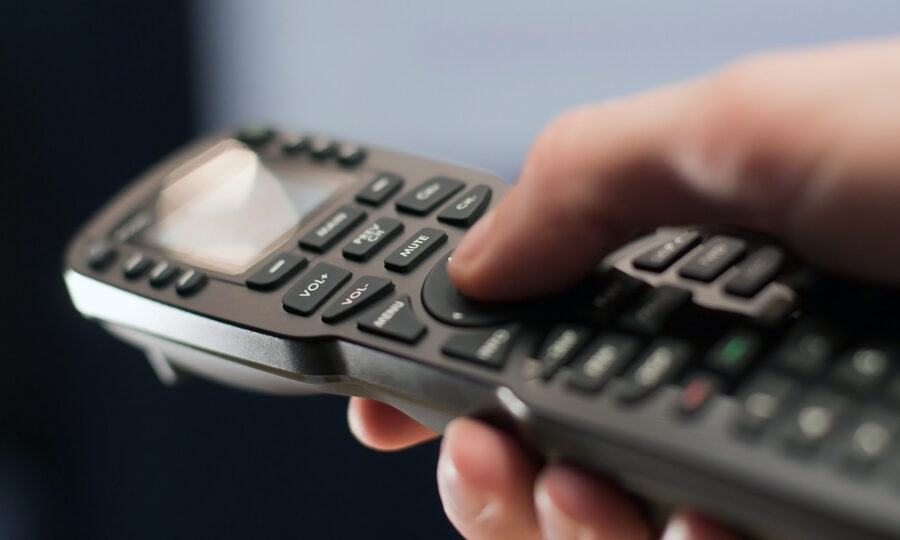 A hand operating a universal-style AV remote control.