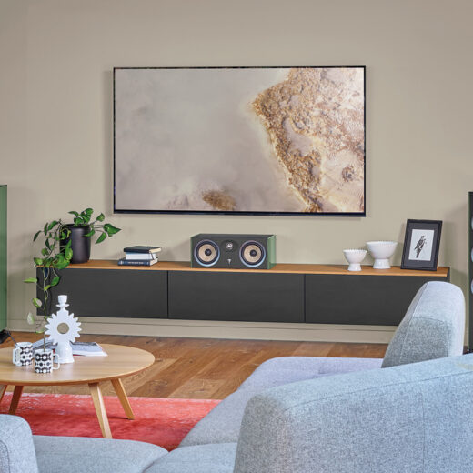 Green Focal Aria Evo X tower speakers and center channel flank a wall-mounted TV in a modern living room.