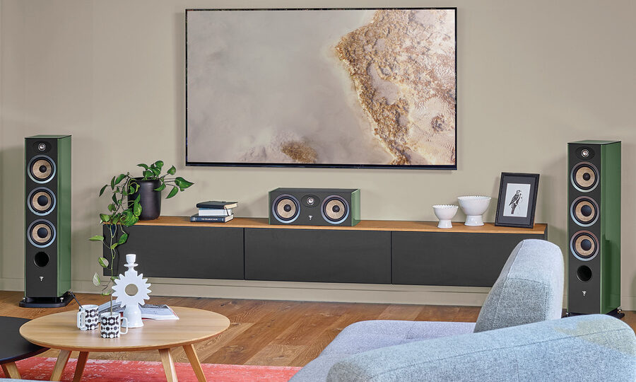 Green Focal Aria Evo X tower speakers and center channel flank a wall-mounted TV in a modern living room.
