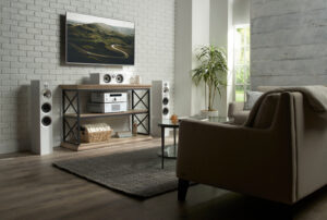 Living room with a wall-mounted TV, white tower speakers, and Rotel stereo components on a console table.