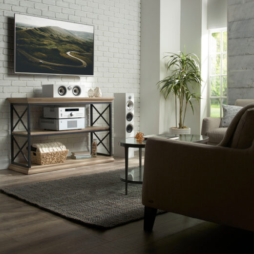 Living room with a wall-mounted TV, white tower speakers, and Rotel stereo components on a console table.