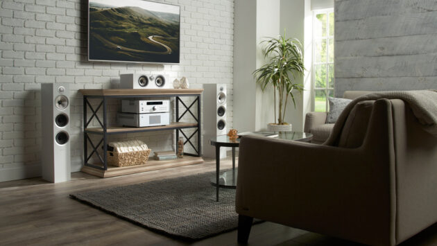 Living room with a wall-mounted TV, white tower speakers, and Rotel stereo components on a console table.