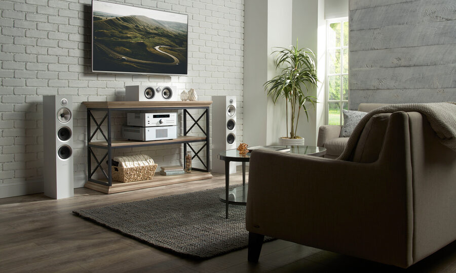 Living room with a wall-mounted TV, white tower speakers, and Rotel stereo components on a console table.
